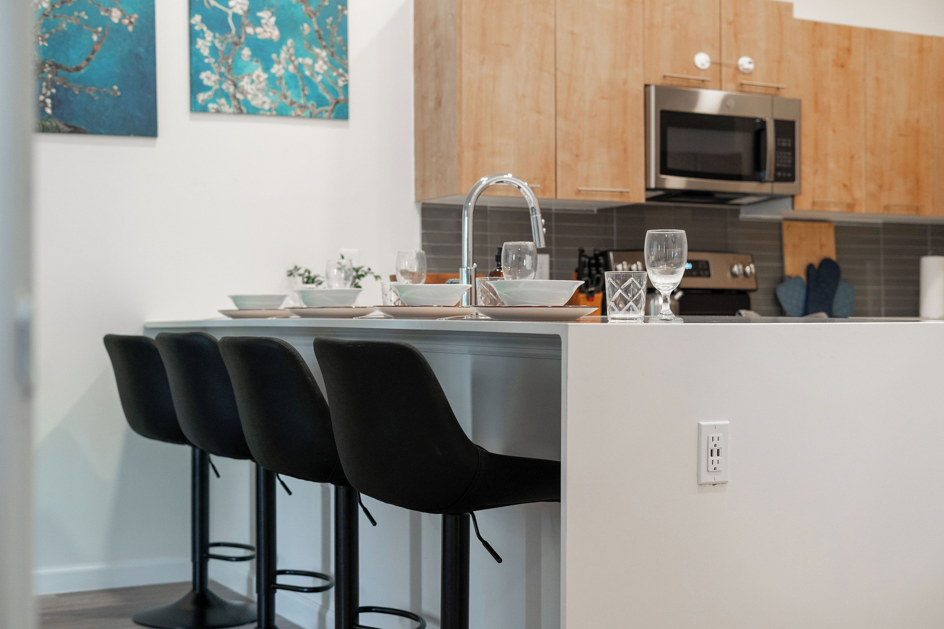 A modern kitchen with a central island, bar stools, a stainless steel microwave, and wooden cabinets.