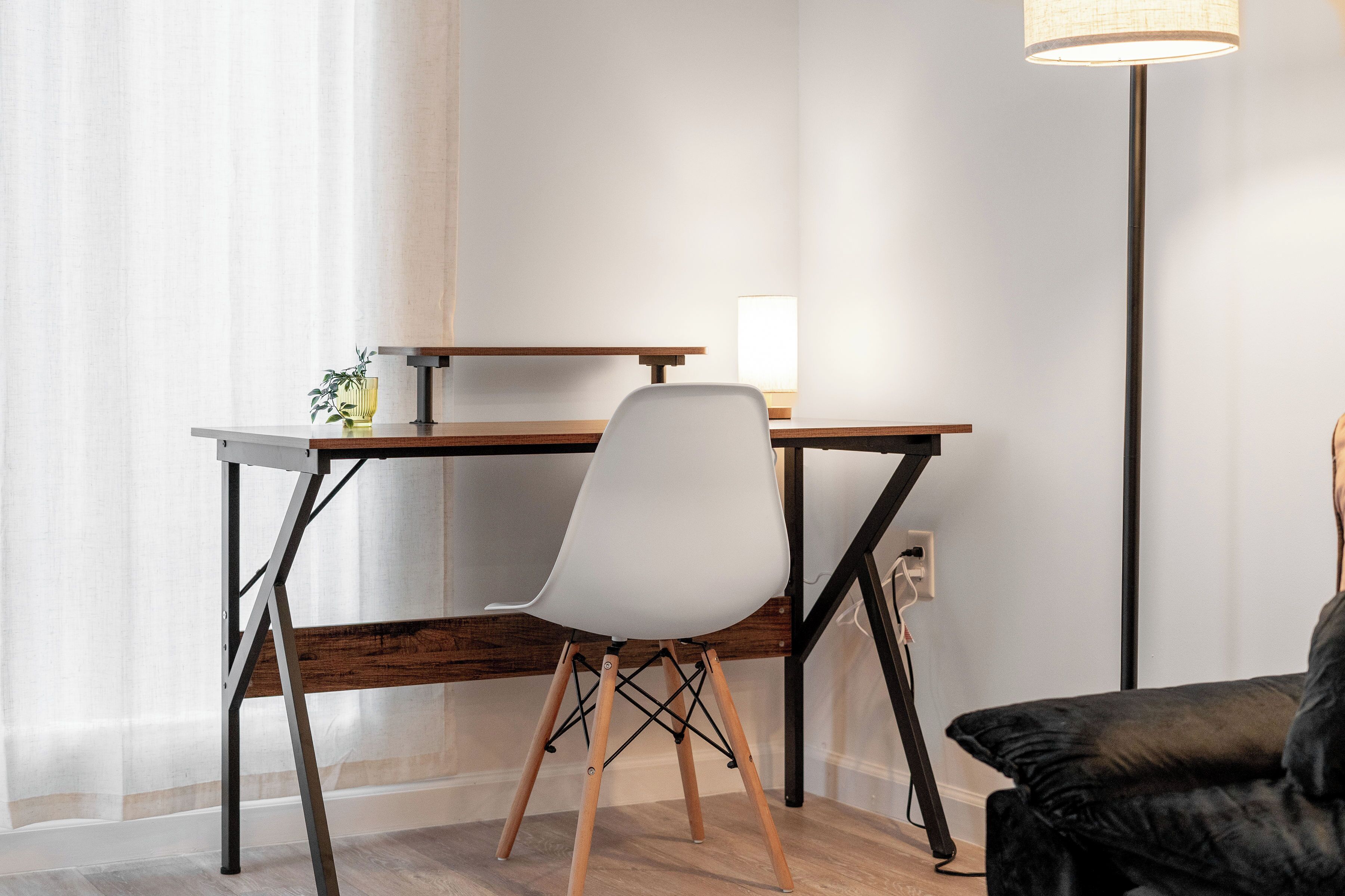 Un espacio de trabajo moderno con escritorio, silla, lámpara y un sofá negro.