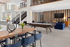 Un moderno vestíbulo de hotel con mesa de billar, zona de estar y una escalera.