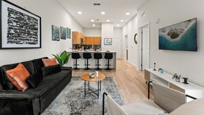 A modern living room with a black sofa, a coffee table, and a kitchen in the background. - Riviere Apartments King Bed Suite & Pool & Gym & Pet Friendly & Near Epic Universe (Orlando)