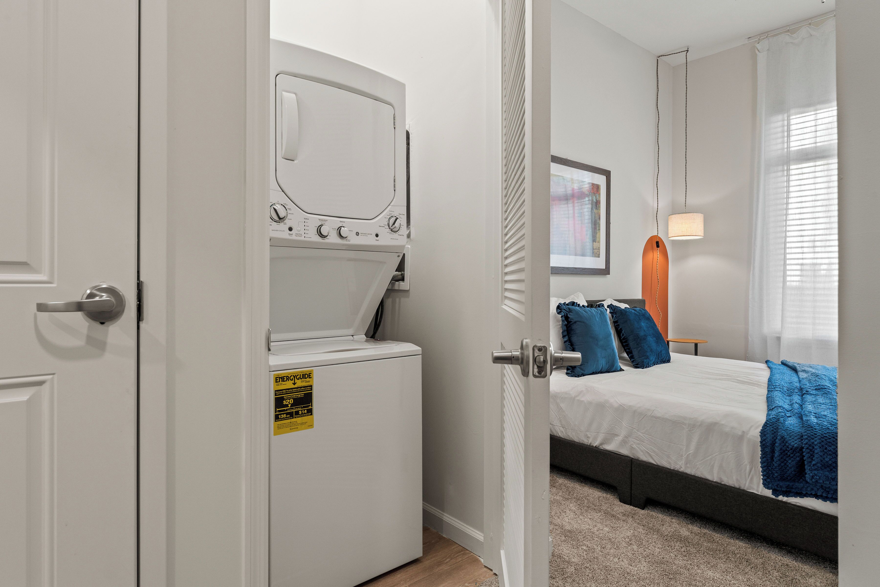 A bedroom with a bed, a washing machine, and a door leading to another room.