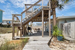 Una terraza de madera que lleva a un edificio con escaleras, mobiliario exterior y una palmera.