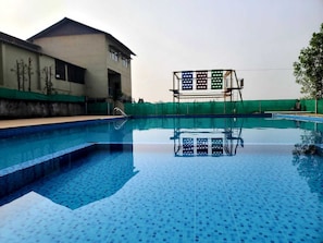 A swimming pool with a tiled deck, a diving board, and a building with a flat roof in the background. - Polo Heritage Resort (Vijayanagar)