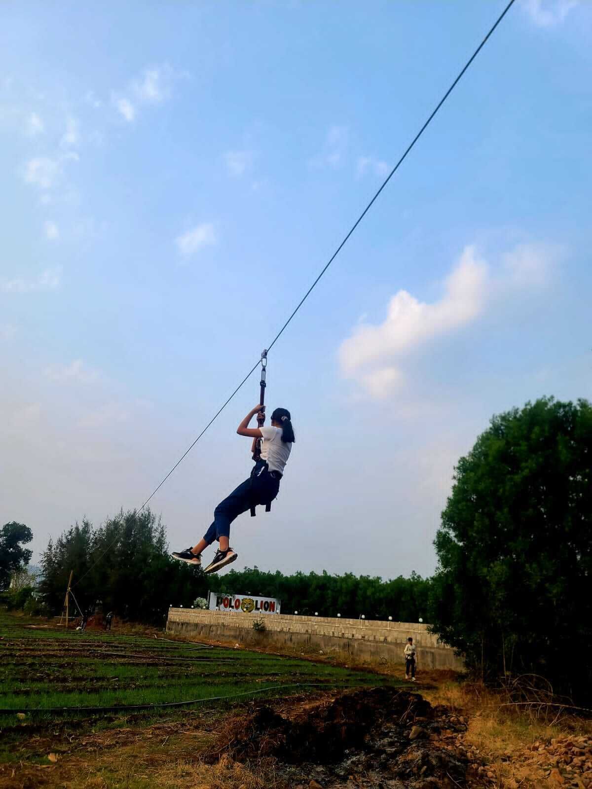 Una persona haciendo tirolesa al aire libre, con cielo despejado y árboles al fondo.