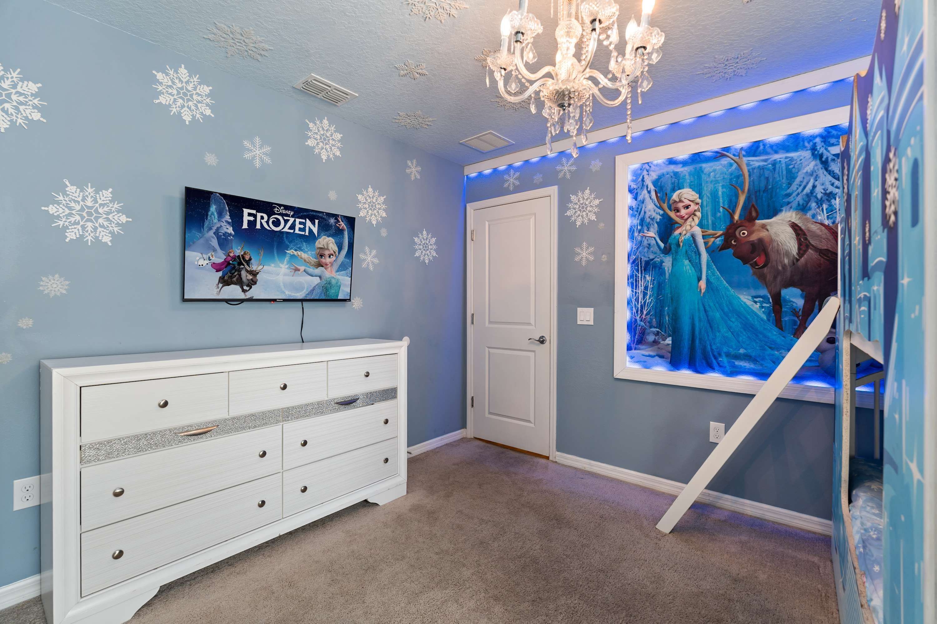 A room with a TV, a dresser, a door, and a wall mural.