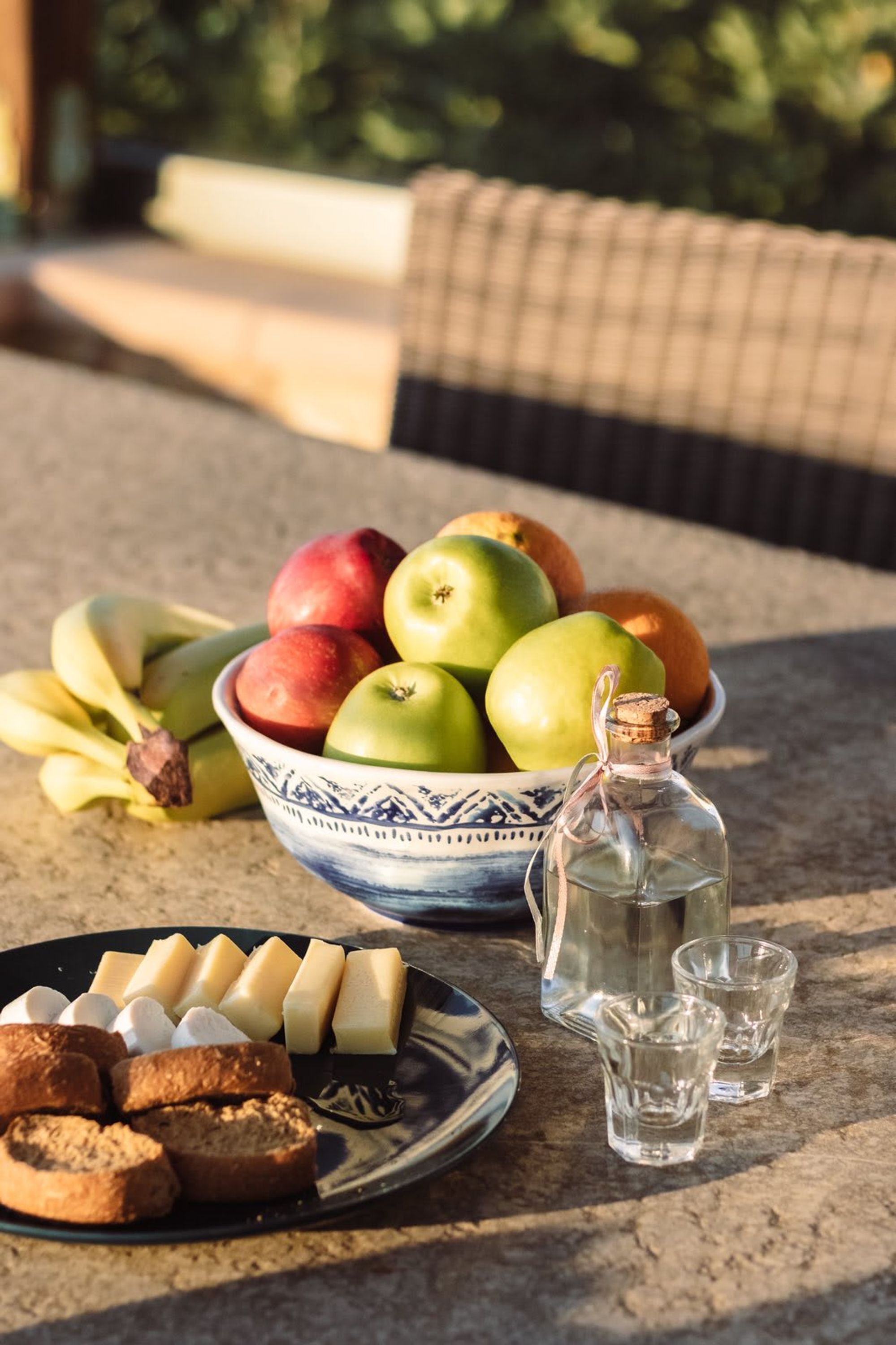 A table with a bowl of fruit, a bottle, and shot glasses.