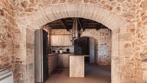 A rustic kitchen with stone walls, a wooden island, and a hanging light fixture. - Vertigo Stone Villa - Roumeli Private Pool Escape (Mylopotamos)