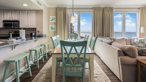 A modern kitchen with a dining area, a sofa, and a view of the ocean. - Gulf-Front Corner Unit with Stunning Panoramic Views (Panama City Beach)