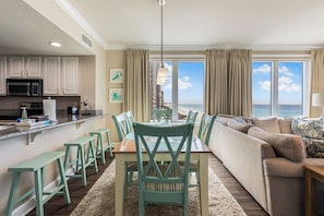A modern kitchen with a dining area, a sofa, and a view of the ocean. - Gulf-Front Corner Unit with Stunning Panoramic Views (Panama City Beach)