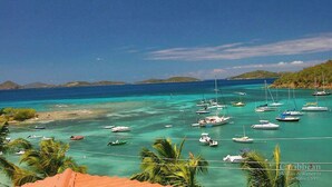 A coastal view with numerous boats anchored in clear turquoise waters, surrounded by lush greenery and distant islands. - Stunning Penthouse at Grande Bay - Breathtaking Views and Luxury Living! (St John)