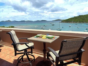 Eine Terrasse mit zwei Stühlen und einem Tisch, mit Blick auf einen Yachthafen, Boote und eine hügelige Landschaft.