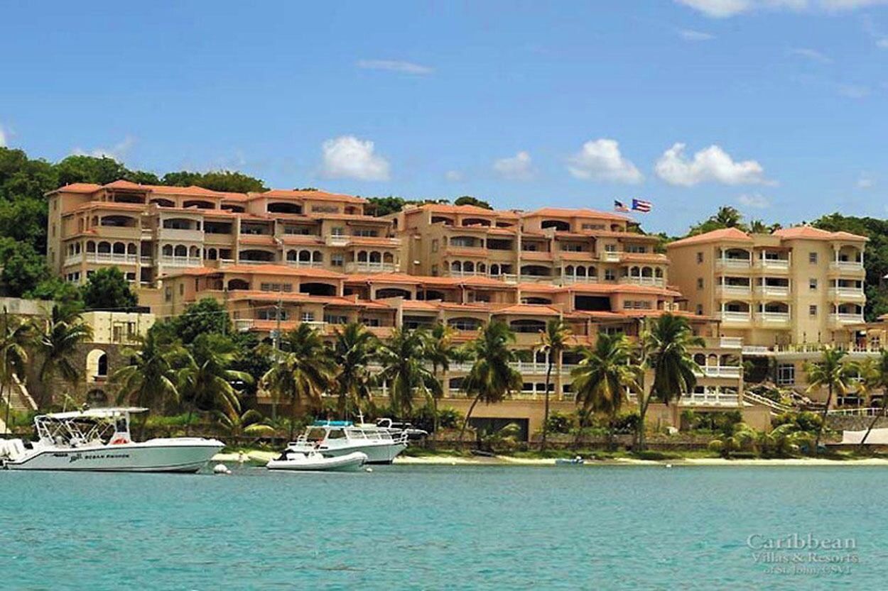 Un hotel frente a la playa con varios balcones, una bandera y varios barcos amarrados en el agua.