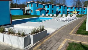 Un área de piscina con sillas de descanso y un edificio de revestimiento azul.