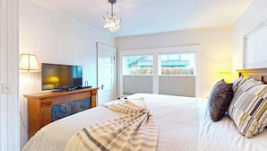 A bedroom with a bed, a television on a wooden cabinet, a star-shaped hanging light, and a window with blinds. - Cozy Cottage at Seaside Beach (Seaside)
