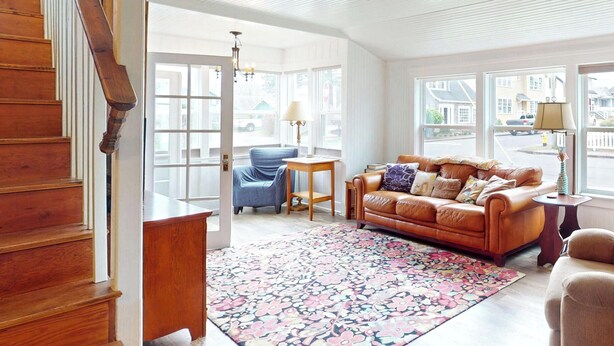 A spacious living room with a wooden staircase, a blue armchair, a brown leather sofa, and a patterned rug. - Cozy Cottage at Seaside Beach (Seaside)