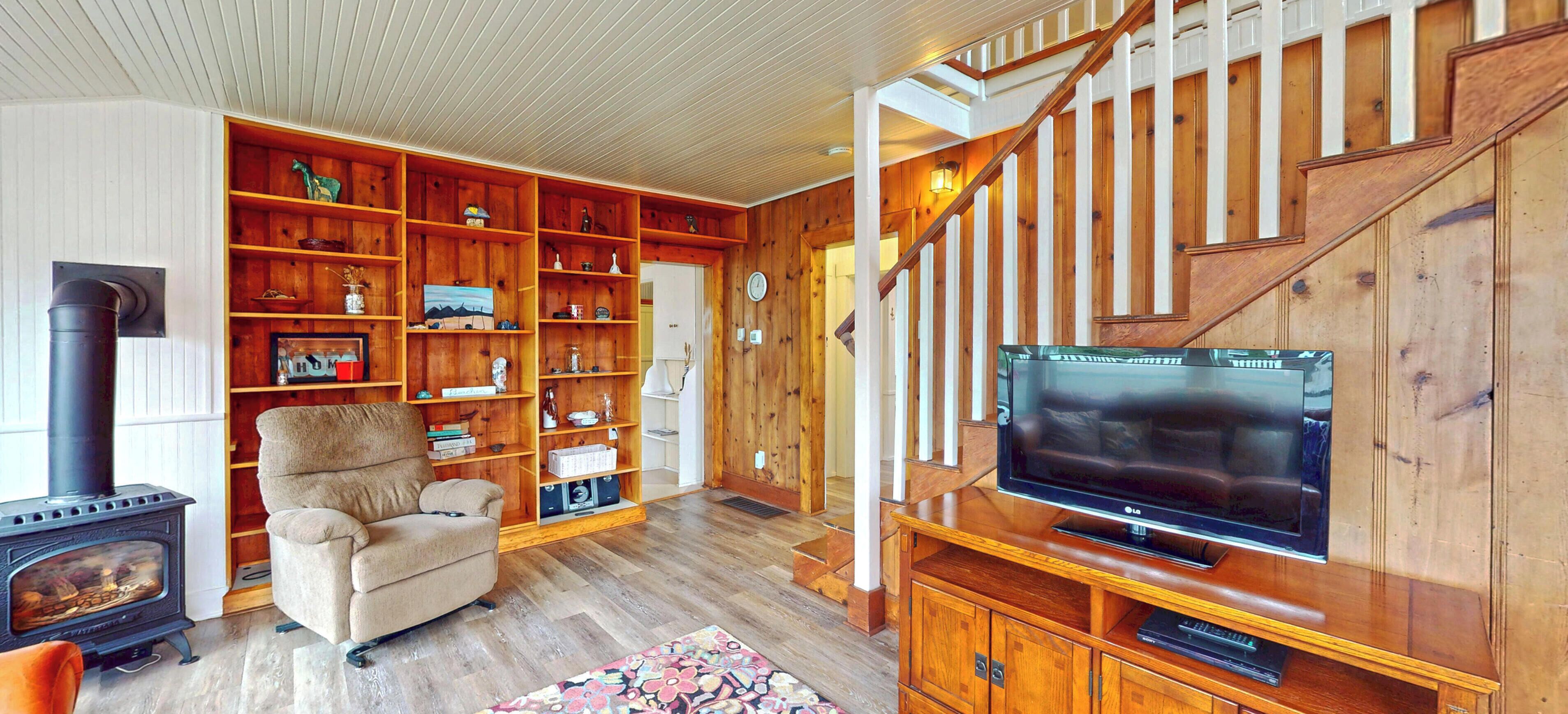 Un salon chaleureux avec une cheminée, un téléviseur, des étagères en bois et un escalier.
