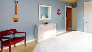 Um quarto com uma cama, cômoda, cadeira, espelho e porta.