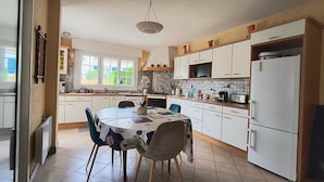 A kitchen with white cabinets, a dining table with chairs, a hanging light fixture, and a refrigerator. - Family home in Parc-Vallière neighborhood, near Royan beach (Royan)