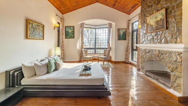 A spacious room with a wooden ceiling, a stone fireplace, a bed with a headboard, and a window with curtains. - Alaya Stays Thistle House 4 BHK Hideaway (Bhimtal)