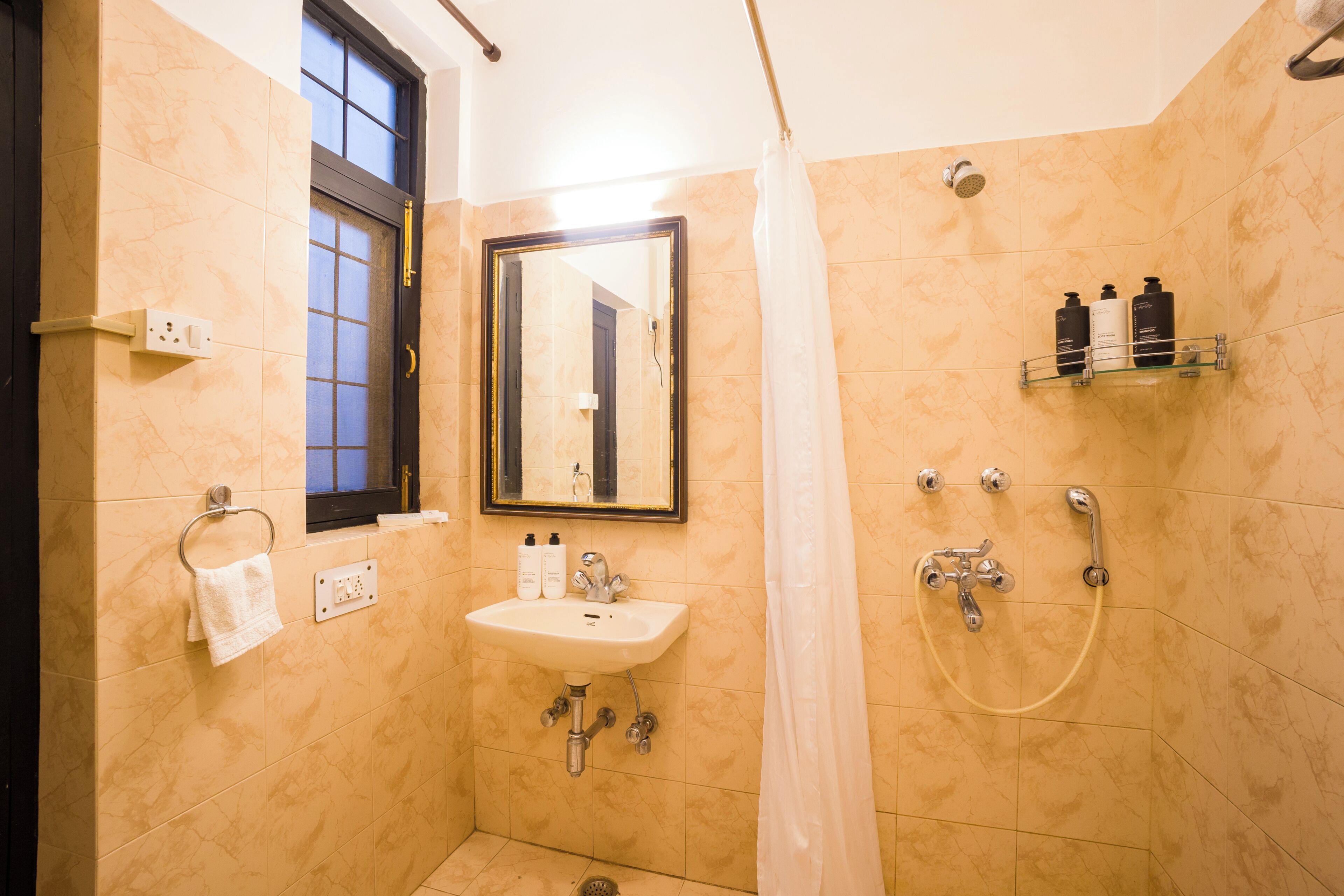 A bathroom with a sink, mirror, shower, and a window.