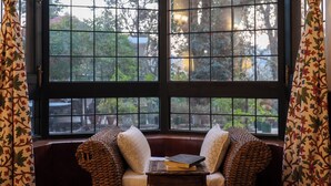 A room with a large window, a cushioned bench with pillows, and a small table with books. - Alaya Stays Thistle House 4 BHK Hideaway (Bhimtal)