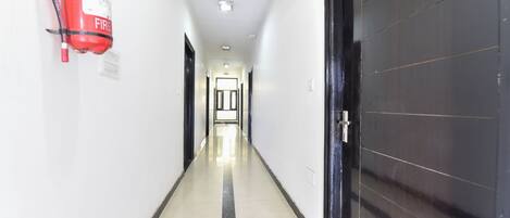 A hallway with a fire extinguisher mounted on the wall, a door with a handle, and a light fixture on the ceiling.