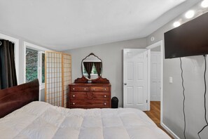 A bedroom with a bed, dresser, mirror, and a TV mounted on the wall. - Forest Cabin Russian River Nature Retreat 2 Bedroom Home (Forestville)