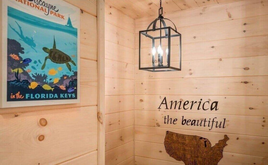 A wooden cabin interior with a poster of a turtle, a hanging light fixture, and a wall map of the USA.