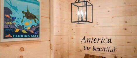 A wooden cabin interior with a poster of a turtle, a hanging light fixture, and a wall map of the USA.