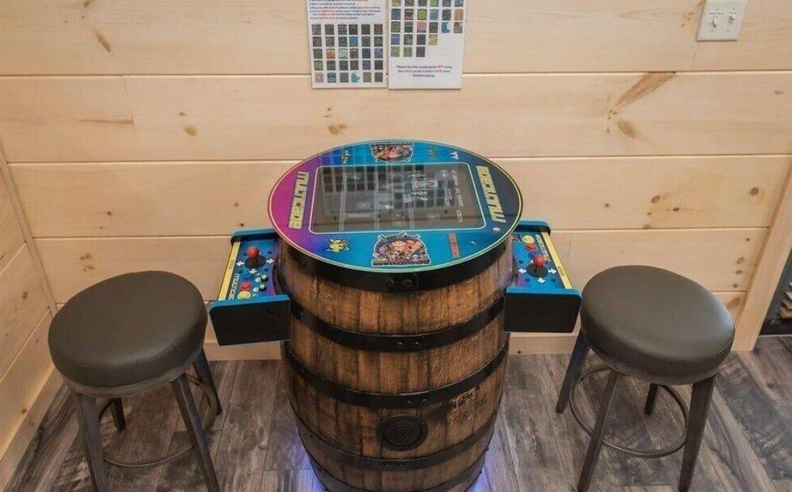 A wooden barrel table with a colorful top, two stools, and a wall-mounted menu board.