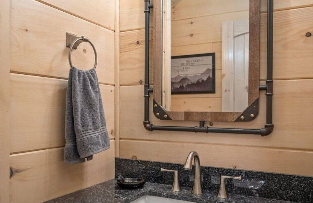 Ein Badezimmer aus Holz mit Handtuchhalter, Spiegel und Waschbecken mit zwei Wasserhähnen.