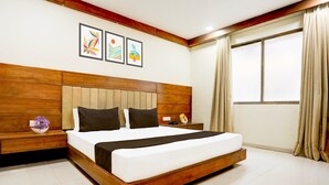 A modern bedroom with a wooden headboard, a large bed with white bedding, a nightstand with a vase of flowers, and a window with curtains. - Super Townhouse Prahladnagar (Ahmedabad)