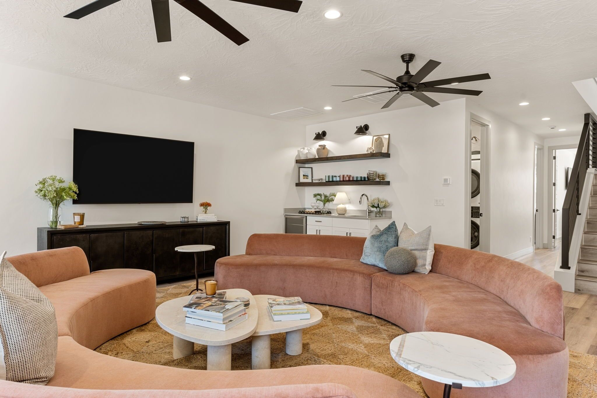 A modern living room with a curved sofa, two coffee tables, a flat-screen TV, and a ceiling fan.