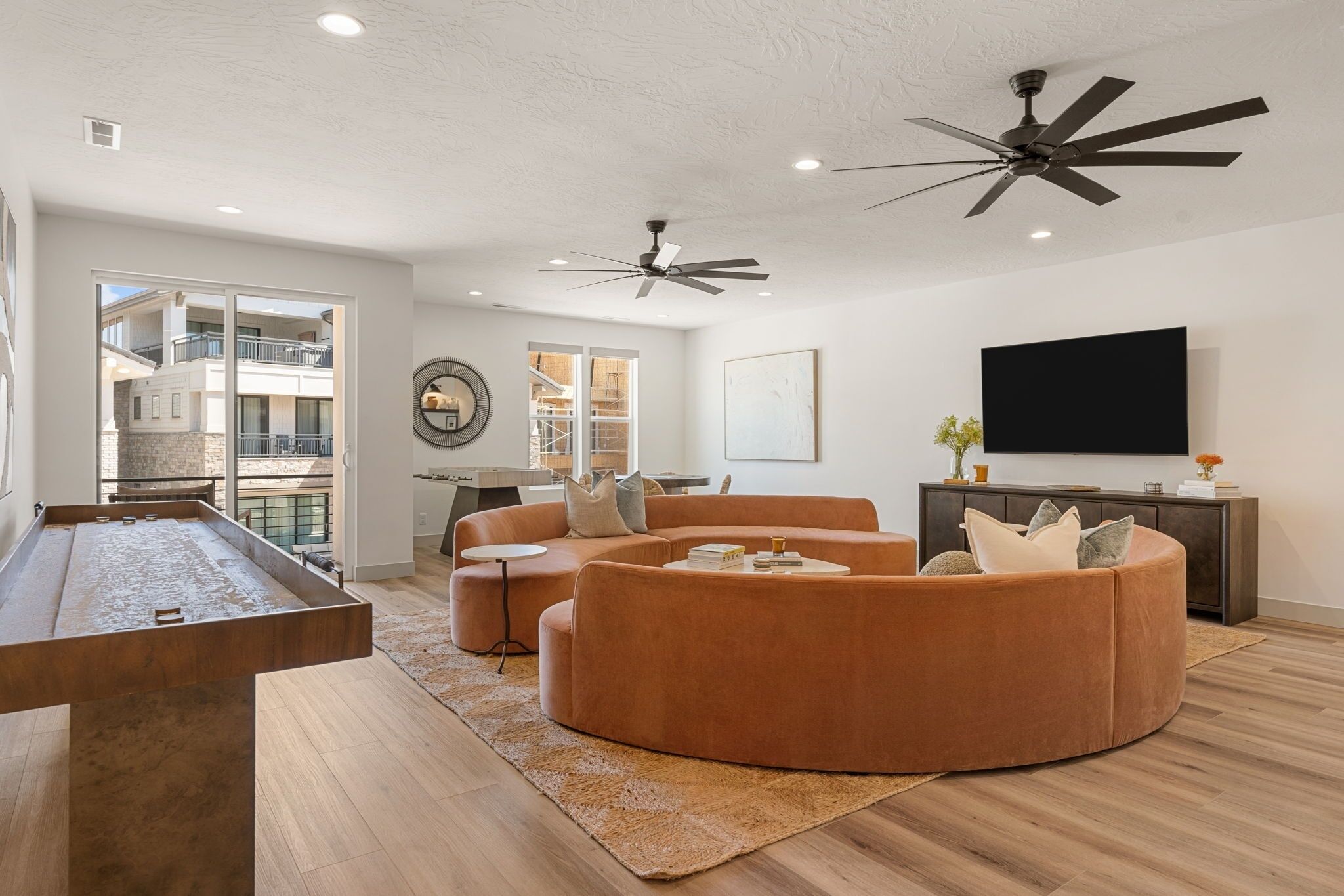Una sala de estar moderna con mesa de billar, sofá modular, ventiladores de techo y televisor de pantalla plana.