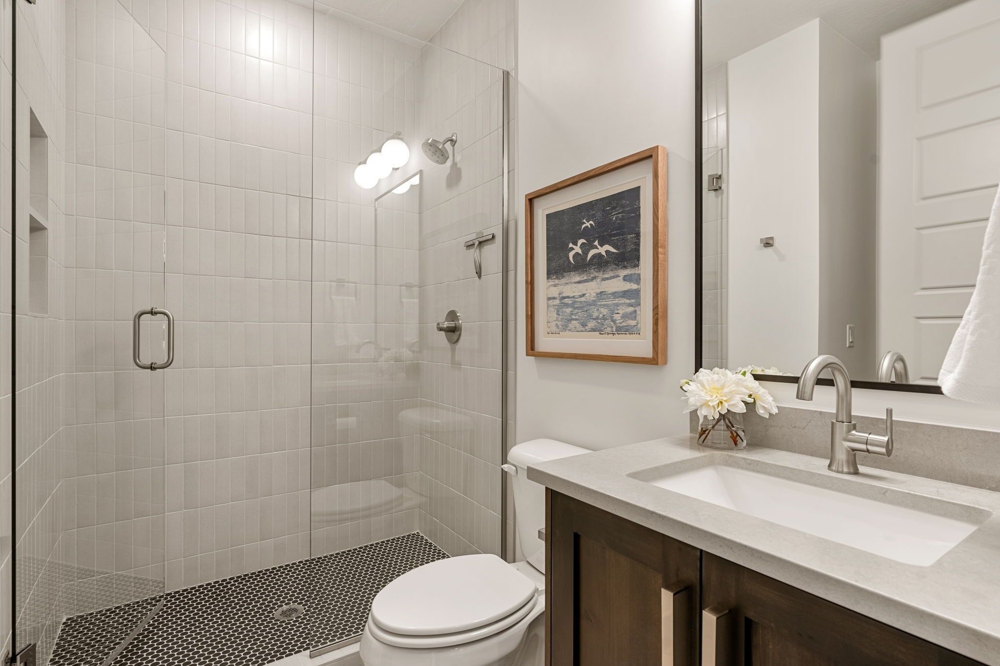 A modern bathroom with a shower, toilet, sink, and a framed picture on the wall.