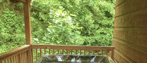A hot tub in a wooden deck area with a view of dense green foliage.