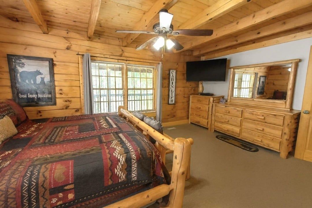 Habitación de cabaña de madera con cama, cómoda, televisor y ventilador de techo.
