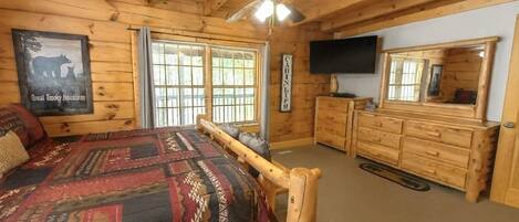 Habitación de cabaña de madera con cama, cómoda, televisor y ventilador de techo.