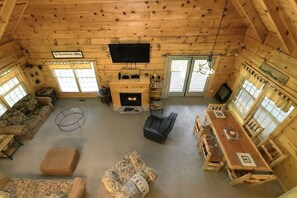 Ein Blockhaus-Interieur mit Kamin, Fernseher und Essbereich.