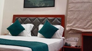 A bedroom with a bed, a nightstand, a wall-mounted air conditioner, a painting, and a window with blinds. - HOTEL VEDIKA  (Ranchi)