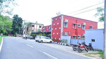 A street with a red building, parked cars, and motorcycles.