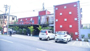 A red building with a sign for a hotel and restaurant, two parked cars, and potted plants. - HOTEL VEDIKA  (Ranchi)