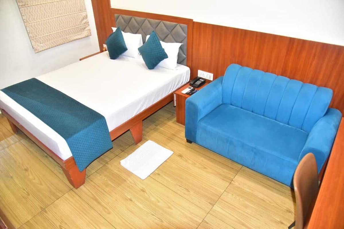 A hotel room with a bed, a blue sofa, a nightstand, and a wooden headboard.