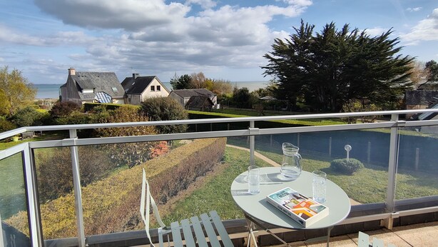 A balcony with a table, chairs, and a glass railing overlooking a garden and houses. - Sea View House for 9 - Beach Just Around the Corner & Family Comfort (Sarzeau)