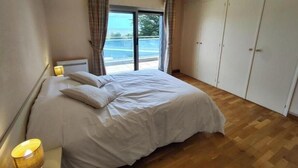 A bedroom with a bed, a bedside lamp, a wardrobe, and a window with curtains. - Sea View House for 9 - Beach Just Around the Corner & Family Comfort (Sarzeau)