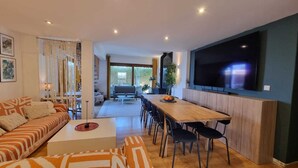 A modern living room with a sofa, coffee table, dining table, and chairs. There is a large flat-screen TV mounted on the wall. - "Villa of Arts".House with the pool, minutes from ocean and not far from Lisbon (Corroios)