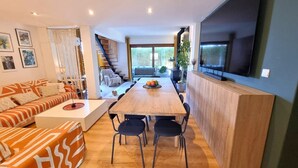 A modern living room with a sofa, a dining table with chairs, a staircase, and a TV mounted on the wall. - "Villa of Arts".House with the pool, minutes from ocean and not far from Lisbon (Corroios)