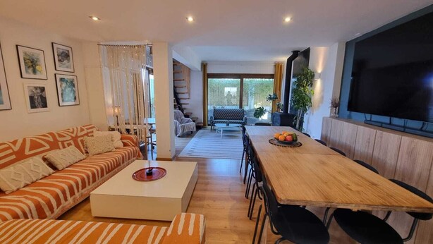 A modern living room with a sofa, coffee table, and dining table. There is a staircase leading to an upper level, and a large window providing natural light. - "Villa of Arts".House with the pool, minutes from ocean and not far from Lisbon (Corroios)
