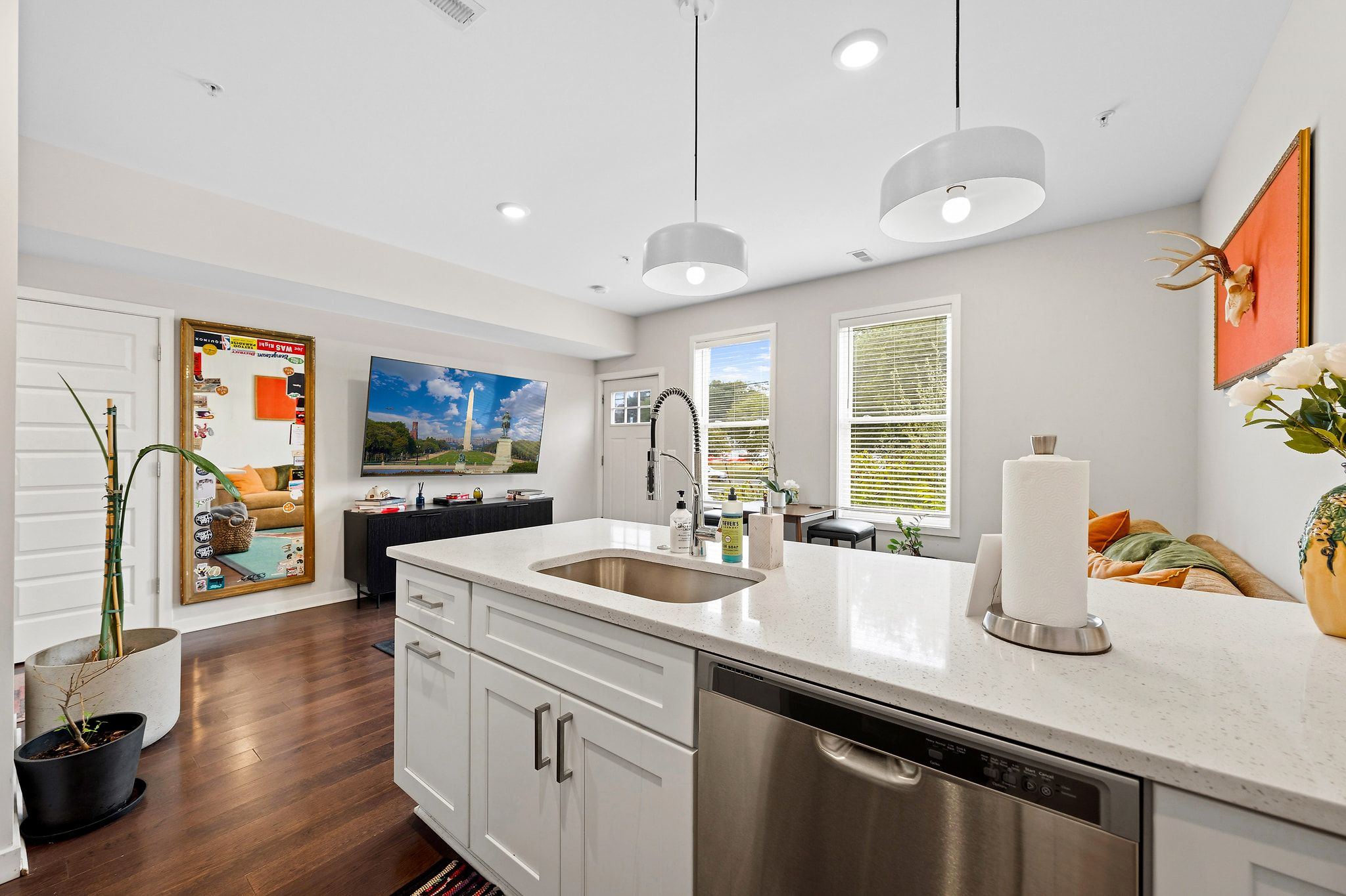 A modern kitchen with a stainless steel dishwasher, a large island with a sink, and pendant lighting.
