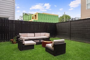 A backyard with a black wooden fence, a green building under construction, and outdoor furniture including a sofa and chairs. - 2BR 2BA DC Oasis Free Parking Near Capitol Hill (Washington)